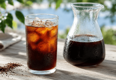 Cold Brew Kaffee im Glas mit Eis neben einer Karaffe und grob gemahlenem Kaffee